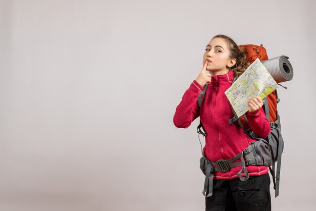 Front view young traveller with big backpack holding up map putting finger on her mouth