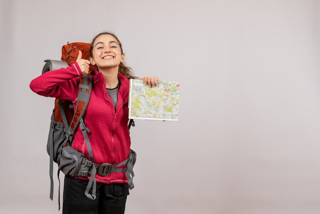 親指をあきらめて地図を指している大きなバックパックを持つ若い旅行者の正面図