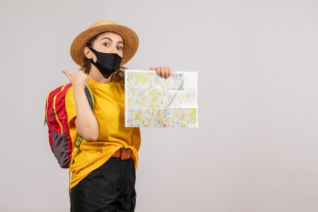 Вид спереди молодой путешественник с красным рюкзаком, держащий карту, показывает палец вверх