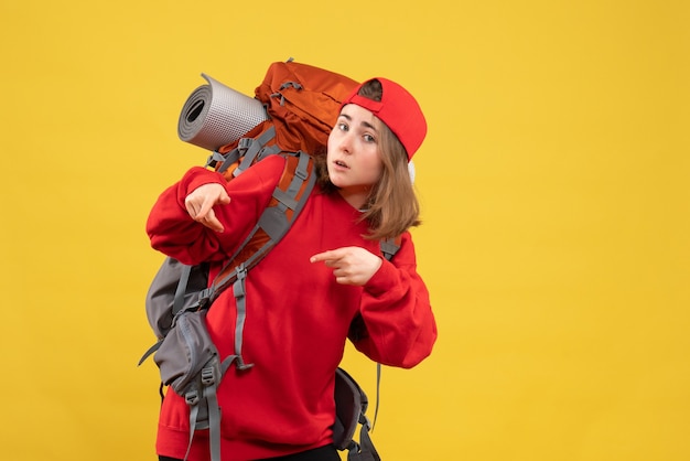 Front view young traveller woman in red backpack standing on yellow wall