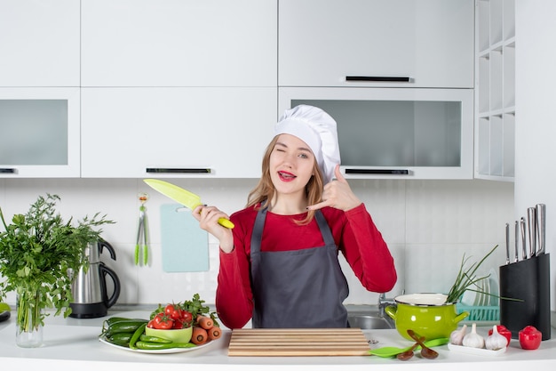 Front view young woman in apron holding up knife making call me sign