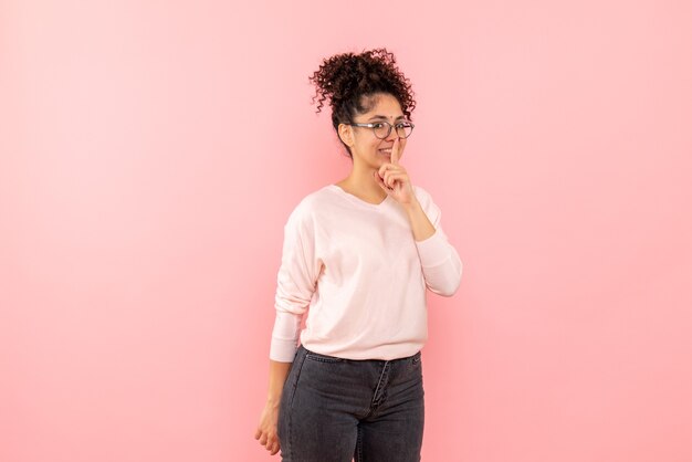 Front view of young woman asking to keep silence on pink wall