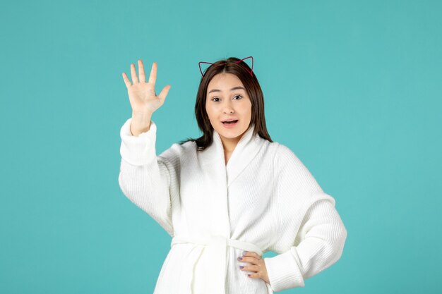 front view of young woman in bathrobe waving on blue wall