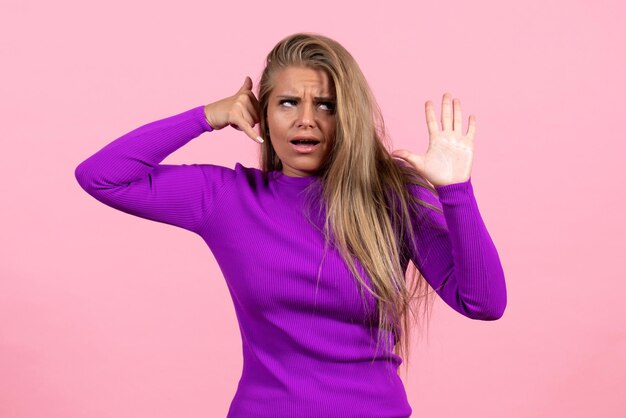 Front view of young woman in beautiful purple dress posing on light pink wall