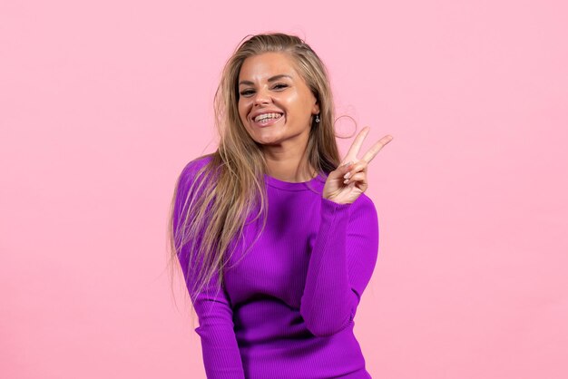 Front view of young woman in beautiful purple dress posing on light pink wall