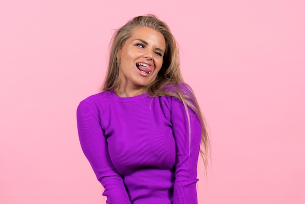 Front view of young woman in beautiful purple dress posing on pink wall