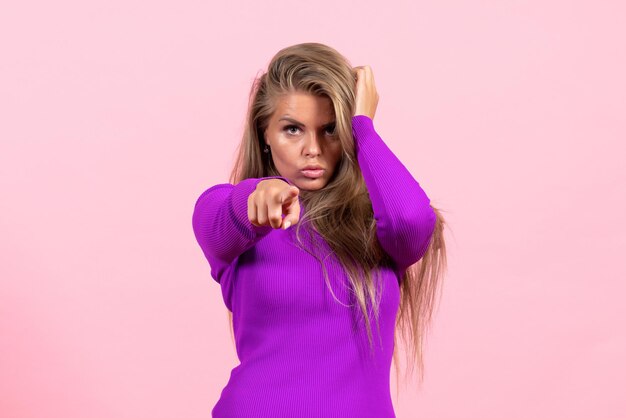 ピンクの壁にポーズをとって美しい紫色のドレスを着た若い女性の正面図