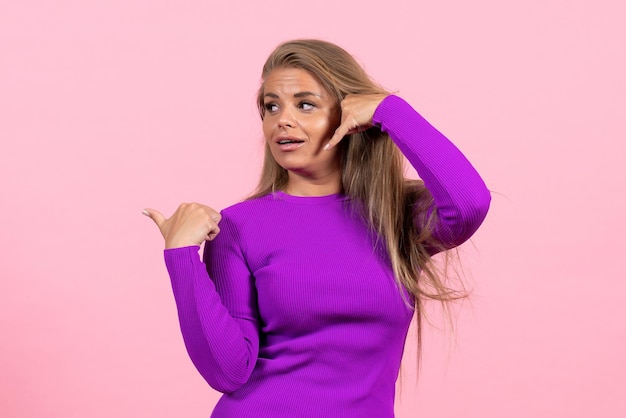 Front view of young woman in beautiful purple dress posing on pink wall