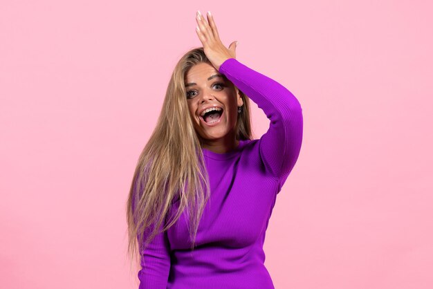 Front view of young woman in beautiful purple dress posing on pink wall