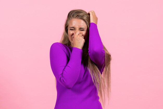 Front view of young woman in beautiful purple dress posing on pink wall