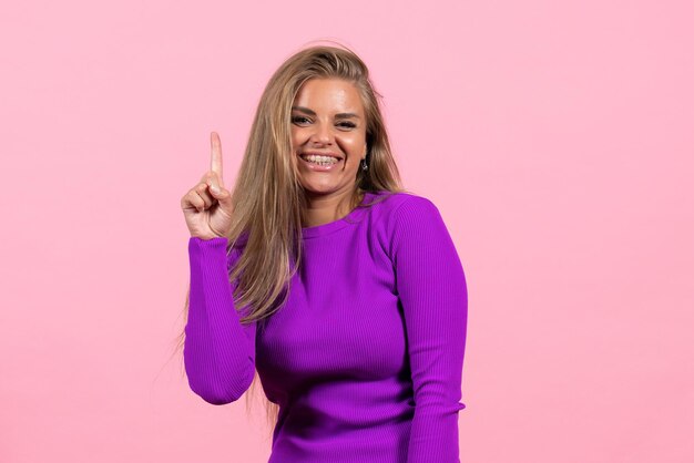 Front view of young woman in beautiful purple dress posing on pink wall