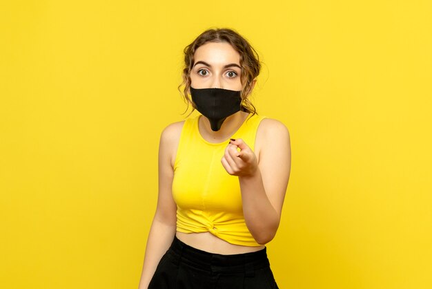 Front view of young woman in black mask surprised on yellow wall