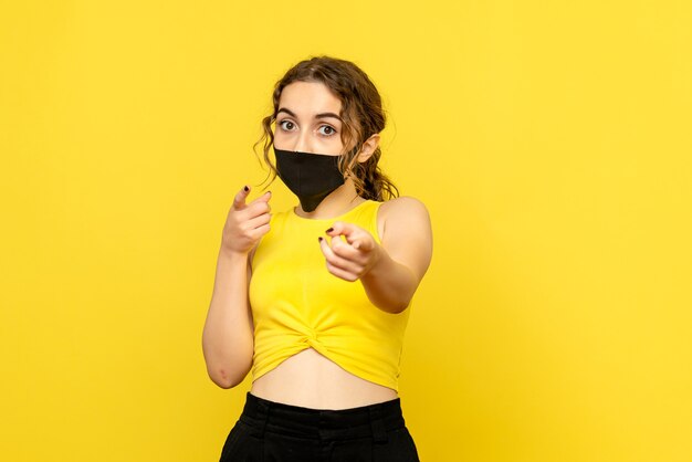 Front view of young woman in black mask on a yellow wall