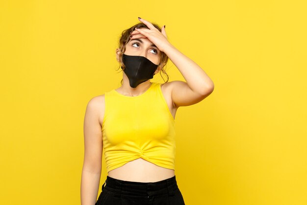 Front view of young woman in black mask on a yellow wall