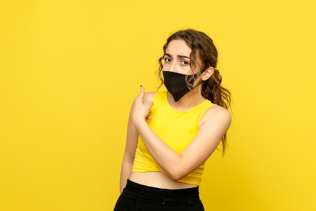 Front view of young woman in black mask on a yellow wall