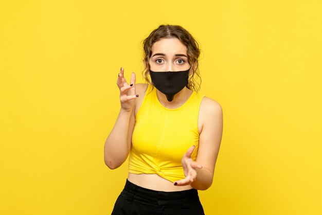 Front view of young woman in black mask on a yellow wall