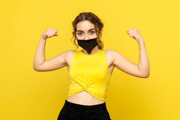 Front view of young woman in black mask on a yellow wall