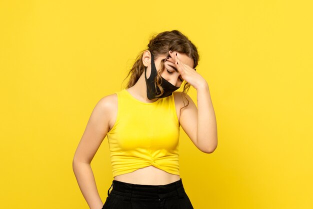 Вид спереди молодой женщины в черной маске на желтой стене