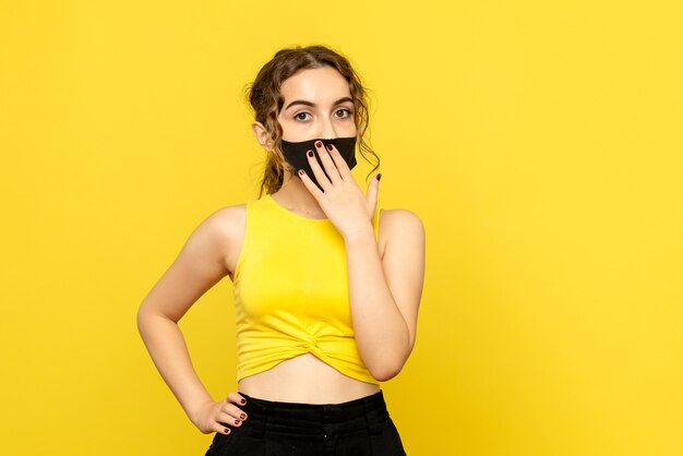 Front view of young woman in black mask on yellow wall