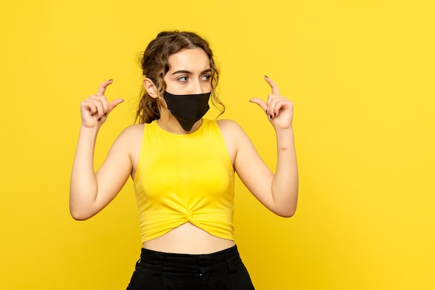 Free photo front view of young woman in black mask on yellow wall