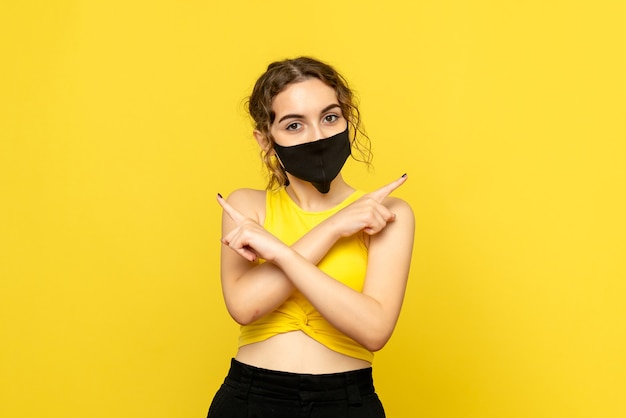 黄色の壁に黒いマスクで若い女性の正面図