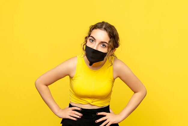 Вид спереди молодой женщины в черной маске на желтой стене