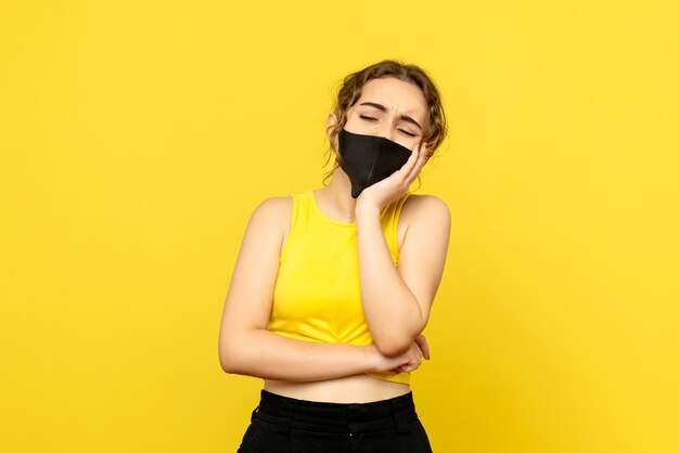 Front view of young woman in black mask on yellow wall