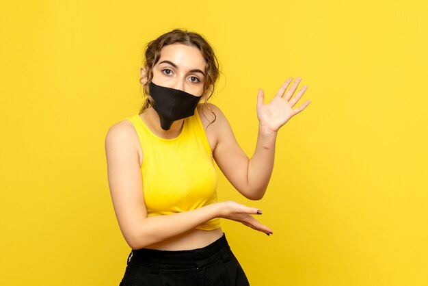 Front view of young woman in black mask on yellow wall