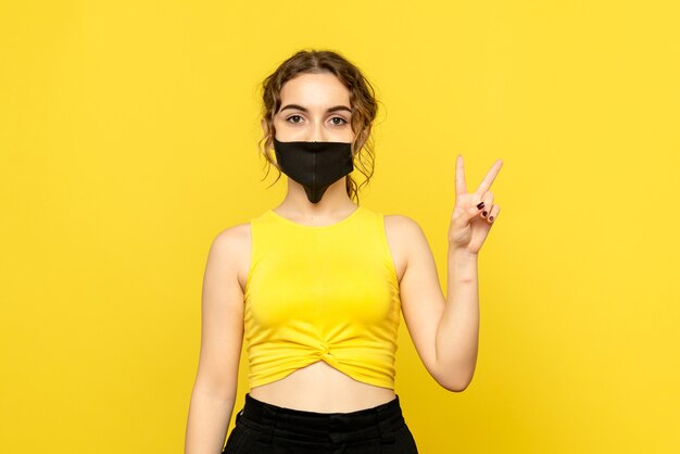 Front view of young woman in black mask on yellow wall