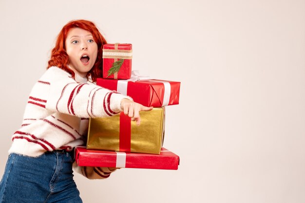 Front view of young woman carrying christmas presents on white wall