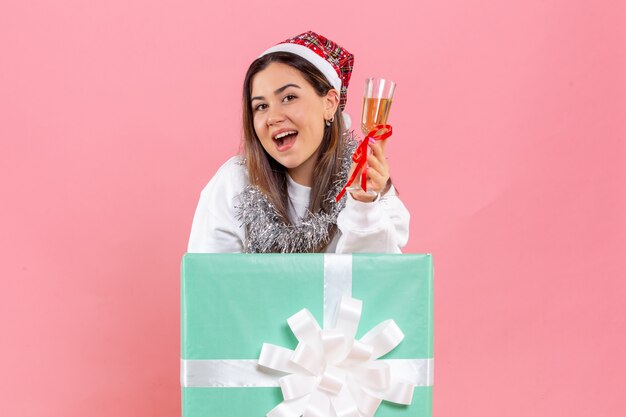 Front view of young woman celebrating xmas with drink on a pink wall