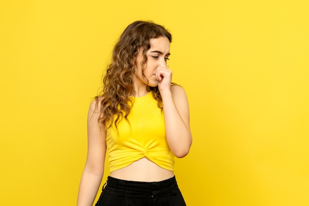 Front view of young woman closing her nose on yellow wall