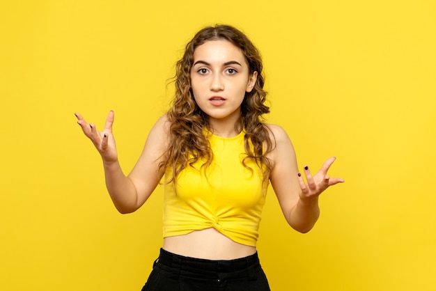 Front view of young woman confused on yellow wall