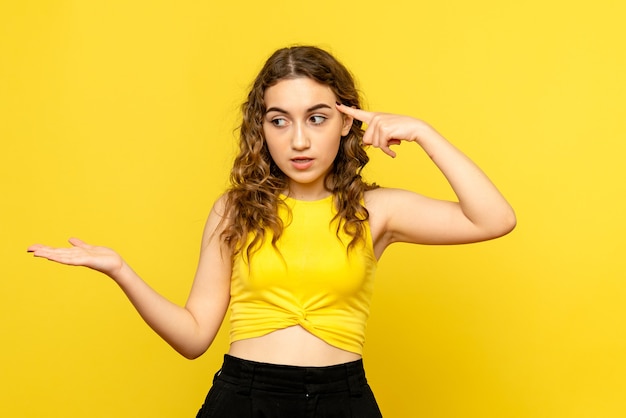 Front view of young woman confused on yellow wall