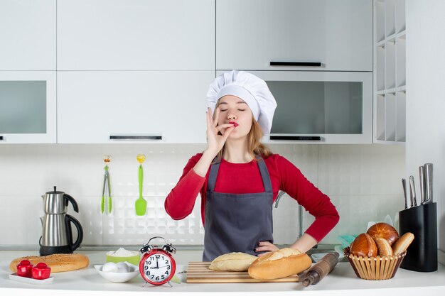 Vista frontale giovane donna con cappello da cuoco e grembiule che fa il bacio del capo in cucina