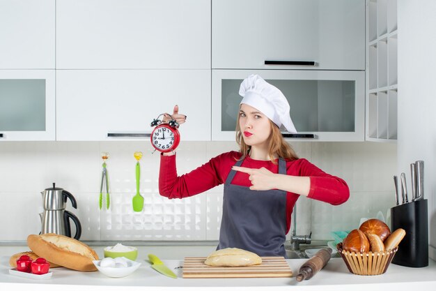 Front view young woman in cook hat holding red alarm clock