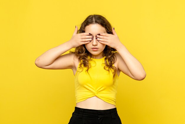 黄色い壁に目を覆っている若い女性の正面図