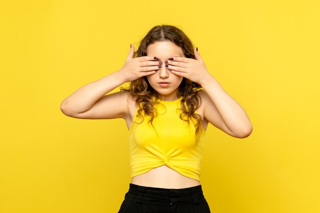 Front view of young woman covering her eyes on yellow wall