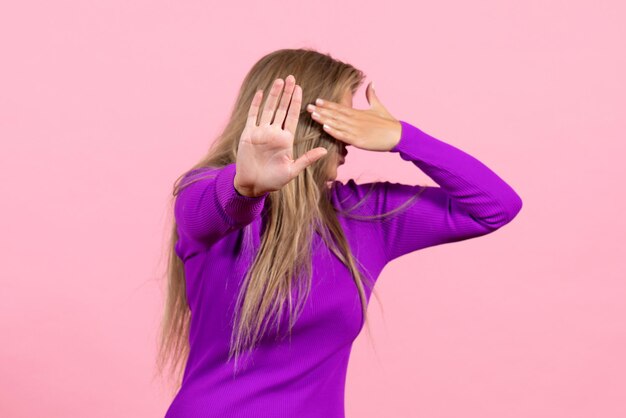 Front view of young woman covering her face in beautiful purple dress on pink wall