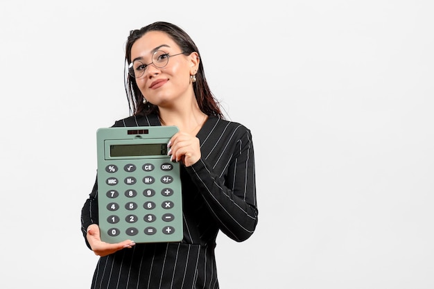 Front view young woman in dark strict suit holding big calculator on a white background beauty business office job fashion