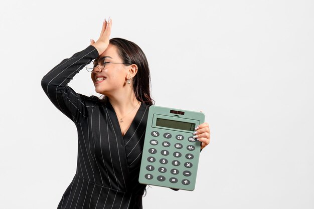 Front view young woman in dark strict suit holding big calculator on white background job beauty woman fashion business office