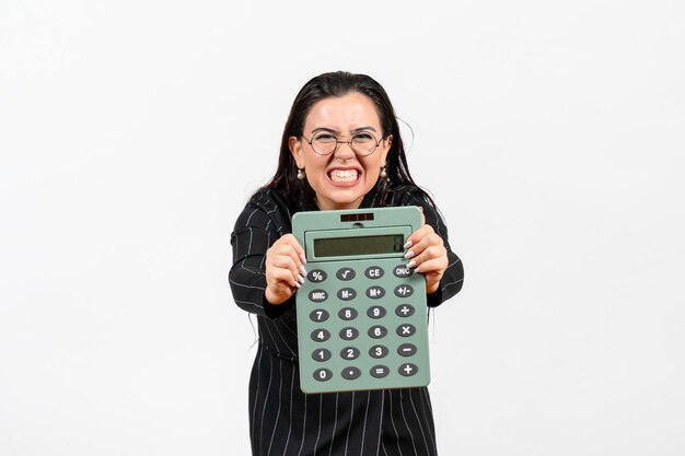 Front view young woman in dark strict suit holding big calculator on the white background office beauty business job fashion female
