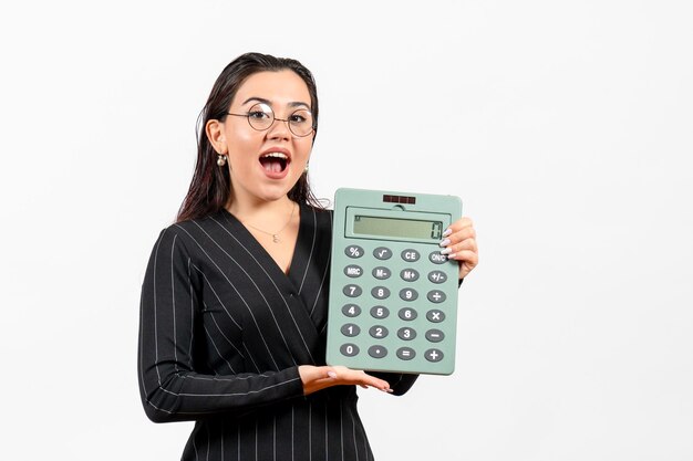 Front view young woman in dark strict suit holding calculator on the white background job woman fashion business beauty office