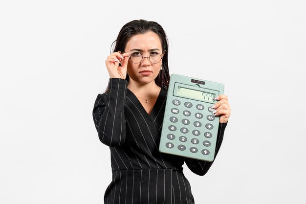 Вид спереди молодая женщина в темном строгом костюме, держащая калькулятор на белом фоне, работа женщина, мода, бизнес, красота, офис