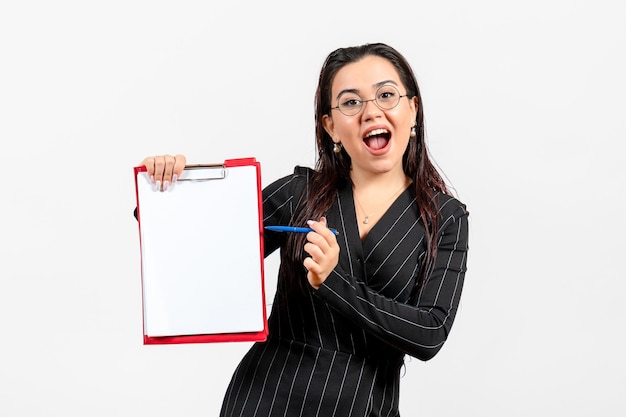 Вид спереди молодая женщина в темном строгом костюме, держащая документ и ручку на белом фоне, деловой женский офисный документ