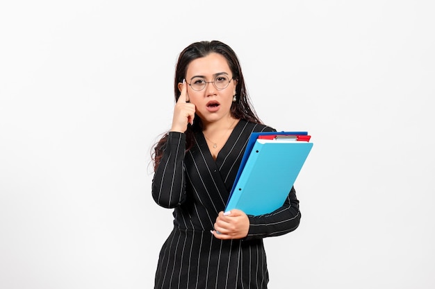 Front view young woman in dark strict suit holding documents on white desk female document business office job