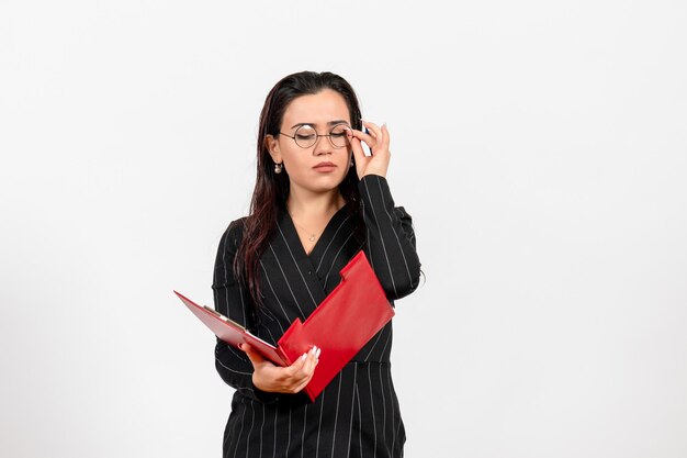 Front view young woman in dark strict suit holding red file on the white background office business job female document