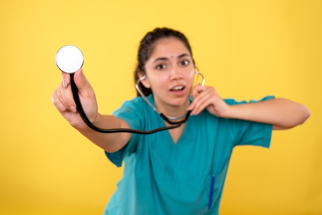 Front view young woman doctor in uniform using stethoscope on yellow background