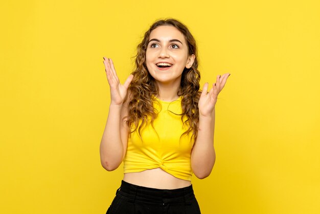 Front view of young woman feeling excited on yellow wall