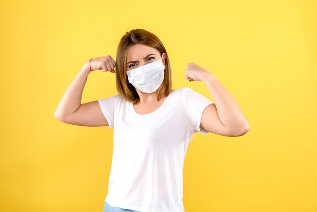 Front view of young woman flexing in mask on yellow wall